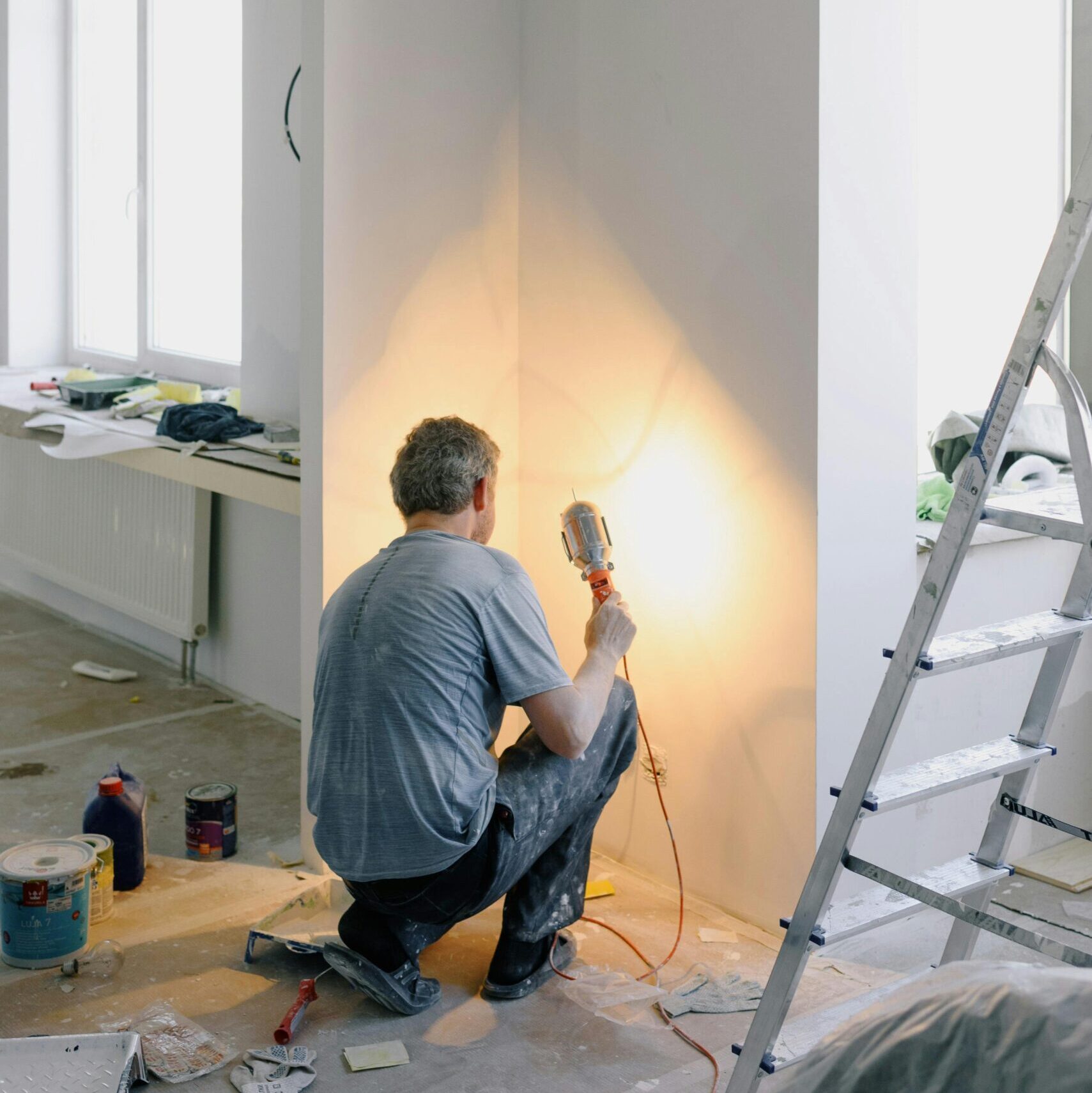 Back view of anonymous male in dirty clothes renovating walls in home while holding lamp